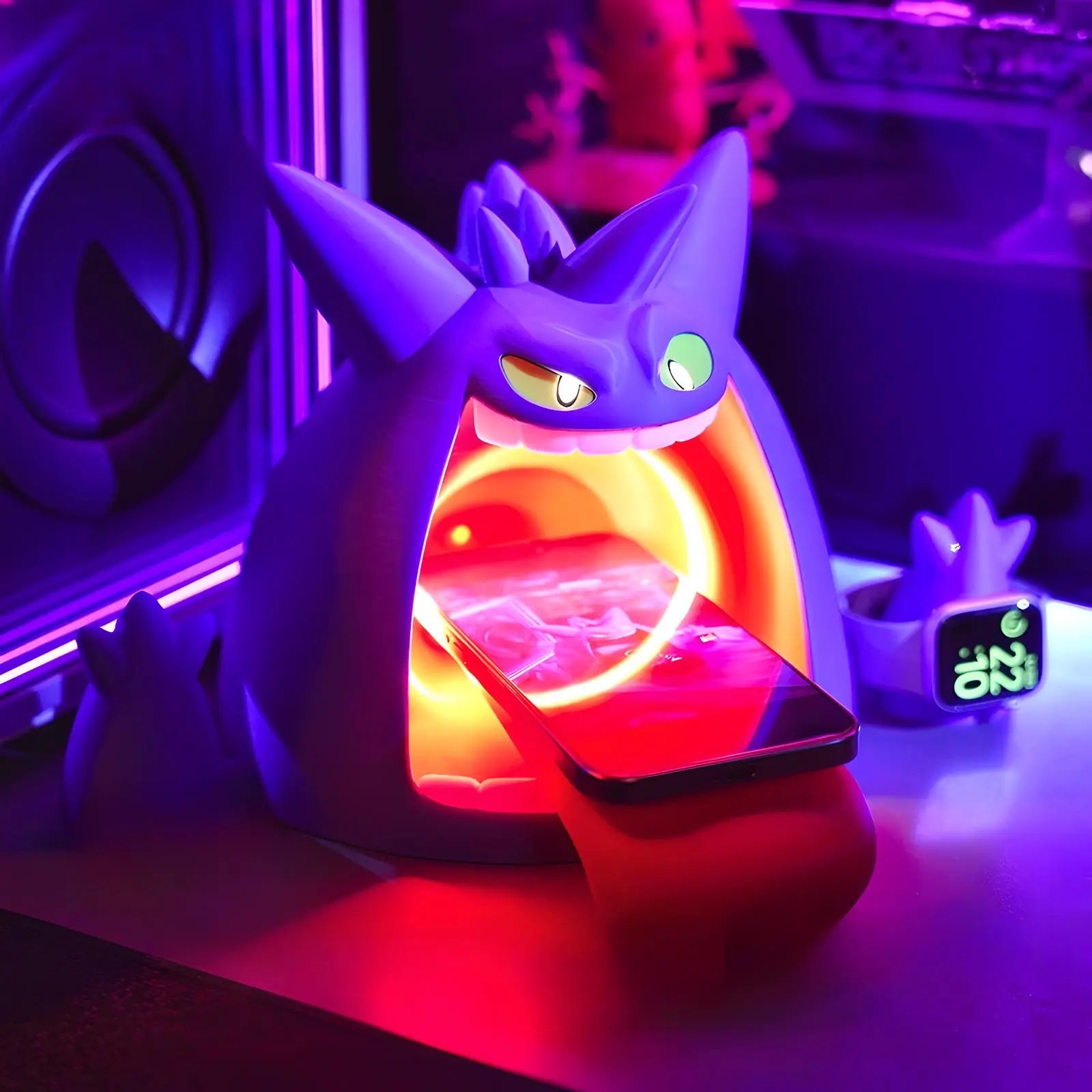Neon desk setup with Gengar-inspired wireless charger, phone charging on angled stand with glowing LED ring, smartwatch dock nearby