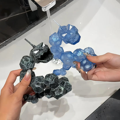 Handheld comparison of black and translucent blue Onix-style toothbrush holder figurines over a sink
